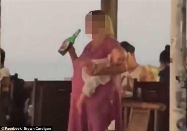 Τουρίστρια κρατάει με το ένα χέρι το μωρό της που κλαίει και με το άλλο πίνει μπύρα